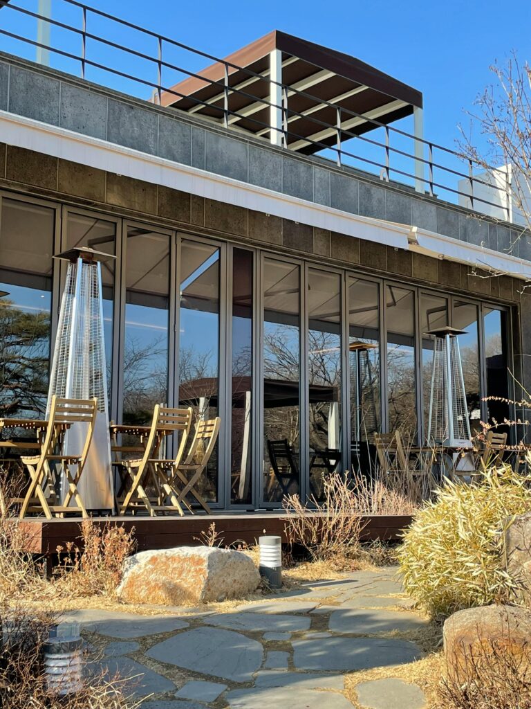 pexels photo 18562519 18562519 Sunny outdoor café with modern architecture, featuring wooden chairs, tables, and patio heaters.